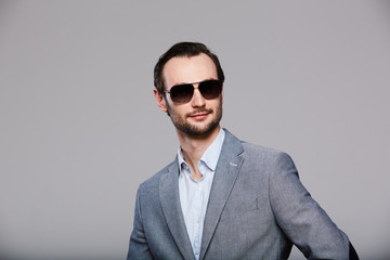 Elegant young handsome man in sunglasses and in stylish gray jacket. Studio fashion portrait.