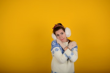 woman in a sweater in gloves hugs herself on a yellow background