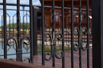 forged iron fence on the bridge over the pond in the park in the summer