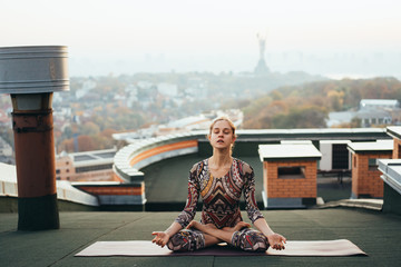 Woman doing yoga on the roof of a skyscraper in big city.