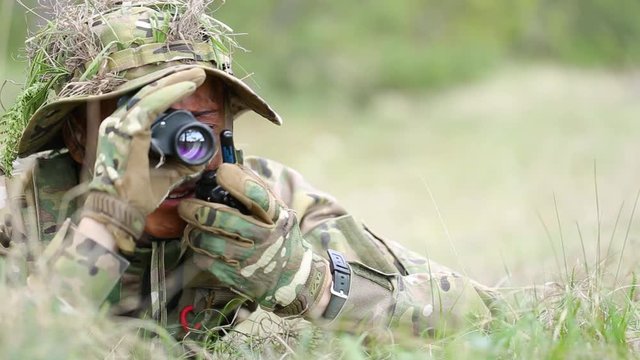 close-up. Camouflage face paint man watching through field glasses. Ghillie suit