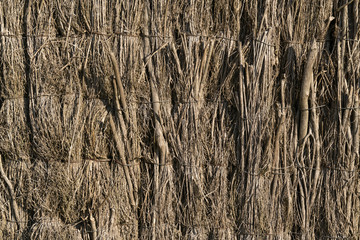 Wall made of bark and twigs held together by metal wire in a bright brown color.