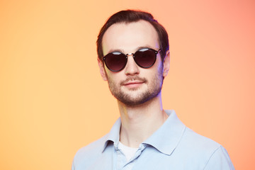 Obraz premium Studio shot of handsome man wearing sunglasses over orange background.