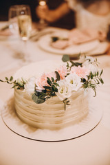 wedding cake stands on a served table and is decorated with flowers