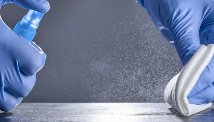 Hands in rubber gloves wipe the table with a disinfectant spray on a grey background. Disinfection...
