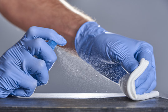 Hands in rubber gloves treat the table with a disinfectant spray on a grey background. Disinfection of premises
