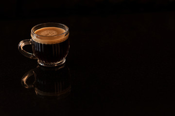 Tasa de vidrio de café expreso sobre fondo de mesa color negro.