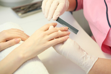 Closeup shot of a woman in a nail salon getting a manicure by a cosmetologist with a nail file. Woman gets a manicure of nails. Beautician puts nails on the client.
