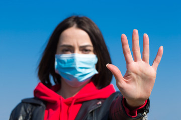 Woman in protective sterile medical mask on her face looking at camera outdoors. Hand stop Sign . Chinese pandemic coronavirus concept.