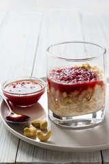 Oatmeal with milk and strawberry jam in glass on white wooden table. healthy organic food. breakfast. close up. vertical layout. copy spice