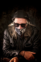 Portrait of a long haired biker wearing leather jacket and leather helmet and sunglasses , leaning...