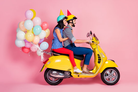 Full size profile side photo positive wife husband two people driver drive yellow choppers anniversary party have air baloons fly wear shirt pants red cone hat isolated pastel color background - Powered by Adobe
