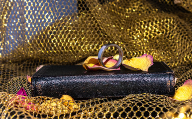 old church hymn book with wedding ring and rose petals and golden fabric as decoration.