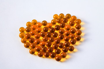 Yellow capsules of vitamins lie on a table on a white background in the shape of a heart