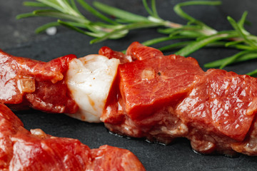 Raw beef kebab with herbs on a dark board, close up