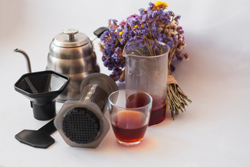 White background, strong, morning, specialty coffee brewed by an alternative method from gadget. Bouquet of field flowers and glassware.