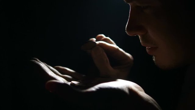 man counts euro coins in dark, carefully examines twists in hands. concept of poverty and unemployment