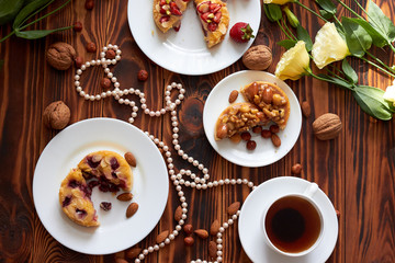 Cup of coffee and three cut mini tarts cupcakes with strawberries, blueberries and with walnuts, almonds and hazelnuts on plate. Top view