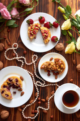 Cup of coffee and three cut mini tarts cupcakes with strawberries, blueberries and with walnuts, almonds and hazelnuts on plate. Top view