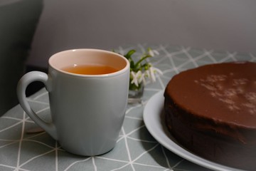 Mug with tea and chocolate cake on the table. Tablecloth with a triangular pattern. Gray green blue color