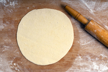Rolled dough on a wooden board sprinkled with flour and rolling pin, pizza dough or