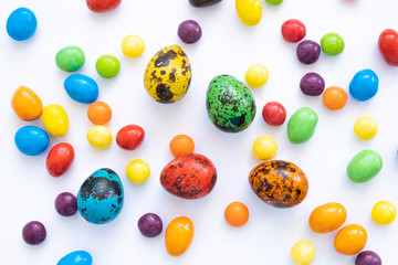 Five multi-colored quail eggs lie among small colored sweets.