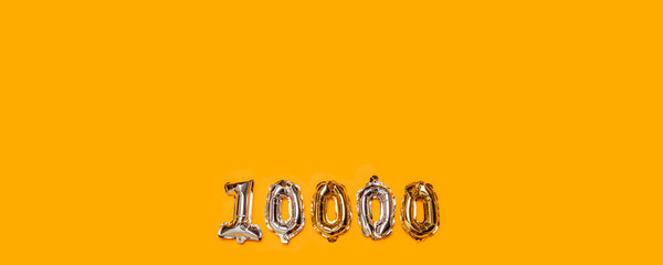 10,000 followers numbers foil balloons on yellow background. Blogger blogging followers concept, top view, flat lay.