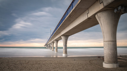 Massive concrete pier leading to horizon surrounded by ocean. Long exposure shot made in New Brighton Beach in Christchurch, New Zealand