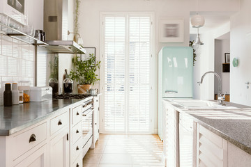 Bright kitchen interior with modern white furniture, pastel mint fridge and big floor to ceiling...