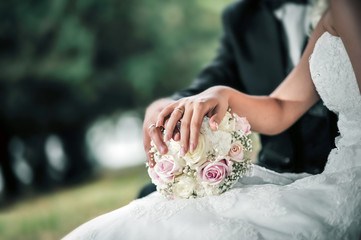 Young married couple holding hands on bouquet of flowers, ceremony wedding day, wedding rings