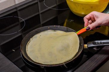 Culinary cook fries pancakes in a pan on an induction stove