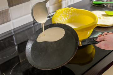 Culinary cook fries pancakes in a pan on an induction stove