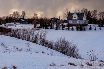 Beautiful winter landscape with a small village on a hill against the backdrop of a sunny sunset in the cloudy sky. Russia, Arkhangelsk region