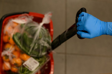 A basket of products in a store. A female hand holds it in a blue protective glove.The concept of protection and disinfection in times of viruses,epidemics, pandemics. Stock of products for quarantine