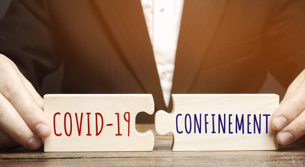 A man collects wooden puzzles with the words Covid-19 and Confinement. Coronavirus pandemic...