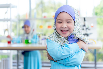 Portrait images of Asian girl 4 year old wearing a blue Islamic dress Smiling and bright with blurred of her friends are studying and doing scientific experiments, to children and education concept.