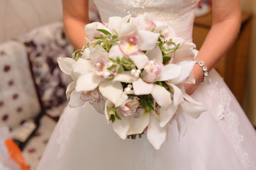 The bride in a white dress holds a beautiful bouquet of orchids