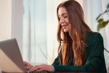 Young, cute business woman sitting in the office and using laptop. Young woman working with a laptop. Female freelancer connecting to internet at home.