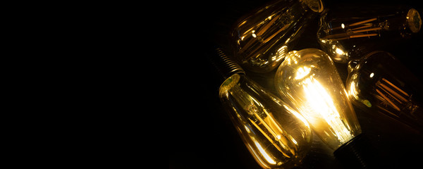 Invention, ideas and leadership concept; Close up glowing lighting bulb on dark black background. Panoramic aspect ratio for copy space. 