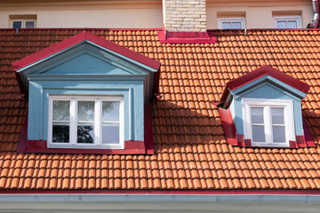 Two windows in latvian jugendstil art nouveau style on roof with orange tiles.