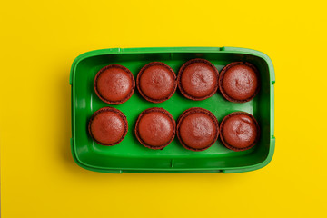 Brown macaroons in plastic box on yellow, top view,