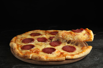Taking slice of tasty pepperoni pizza on black table