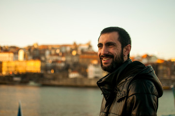 warm man with black jacket, smiles, posing against the background of the city and house of Porto, in the boat area, Portugal