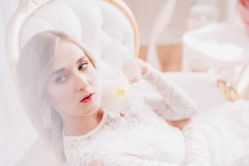 Beautiful bride in a white laced dress and wedding bouquet  is preparing for wedding ceremony in hotel room. Bride getting ready. Artwork