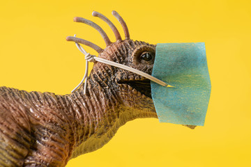 Close up o a plastic dinosaur toy with face mask on yellow background