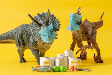 Two plastic dinosaurs with face masks and groceries on yellow background © gogajuice