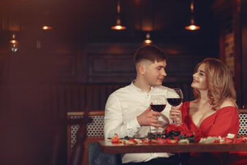 Couple in a restaurant. Lady in a red dress. Pair drinking a vine. Valentine's day.