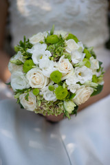 The bride in a white dress holds a beautiful bouquet of white delicate roses