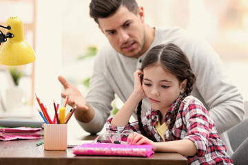 Father scolding his daughter while helping with homework at table indoors