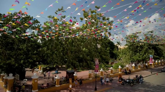 Camera panning right showing the cathedral San Gervasio and the Zocalo, or central park with flag waving in Valladolid, Yucatan, Mexico.